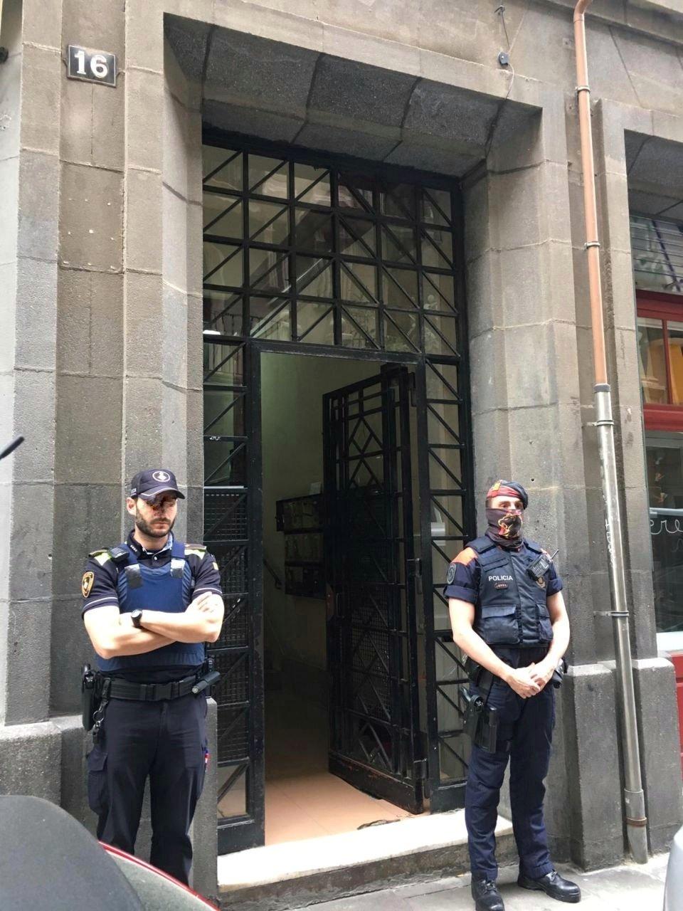 Un agent de la Guàrdia Urbana i els Mossos a la porta de l'edifici.| GUB