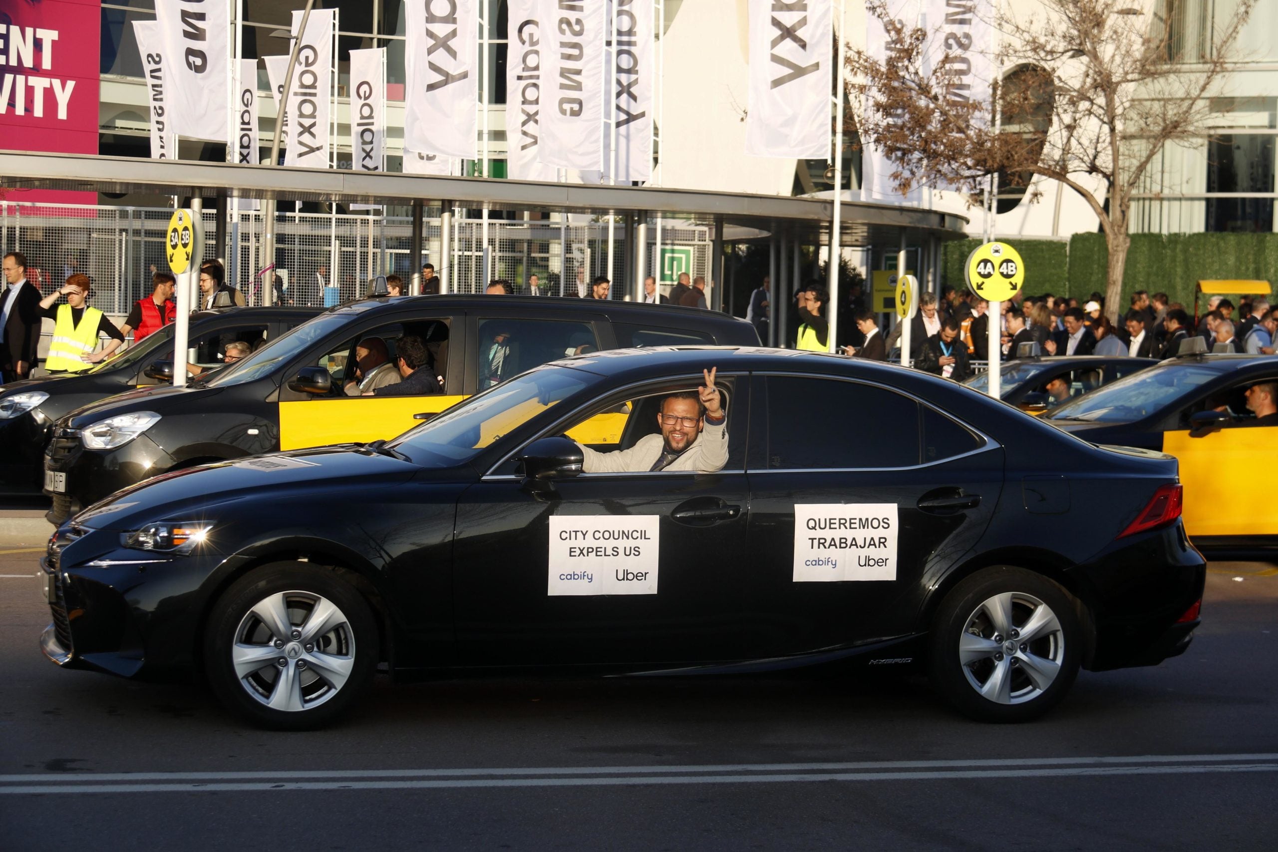 Un VTC amb un cartell on hi posa 'volem treballar', amb taxis de fons / ACN