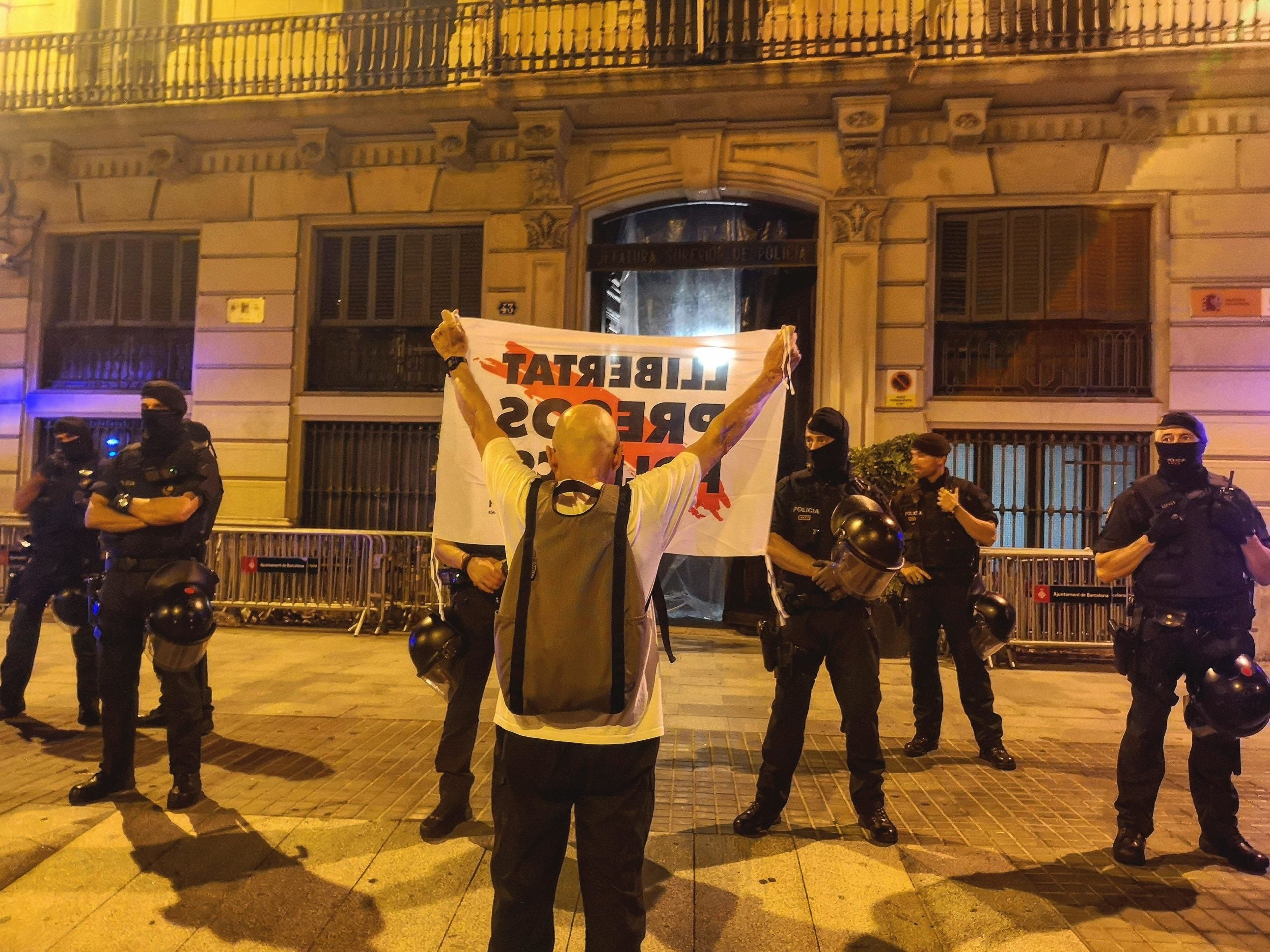 Un manifestant ensenya una pancarta en defensa dels presos polítics als mossos que protegeixen la prefectura de la Policia Nacional, a la Via Laietana, en la protesta contra l'empresonament dels CDR / D.C.