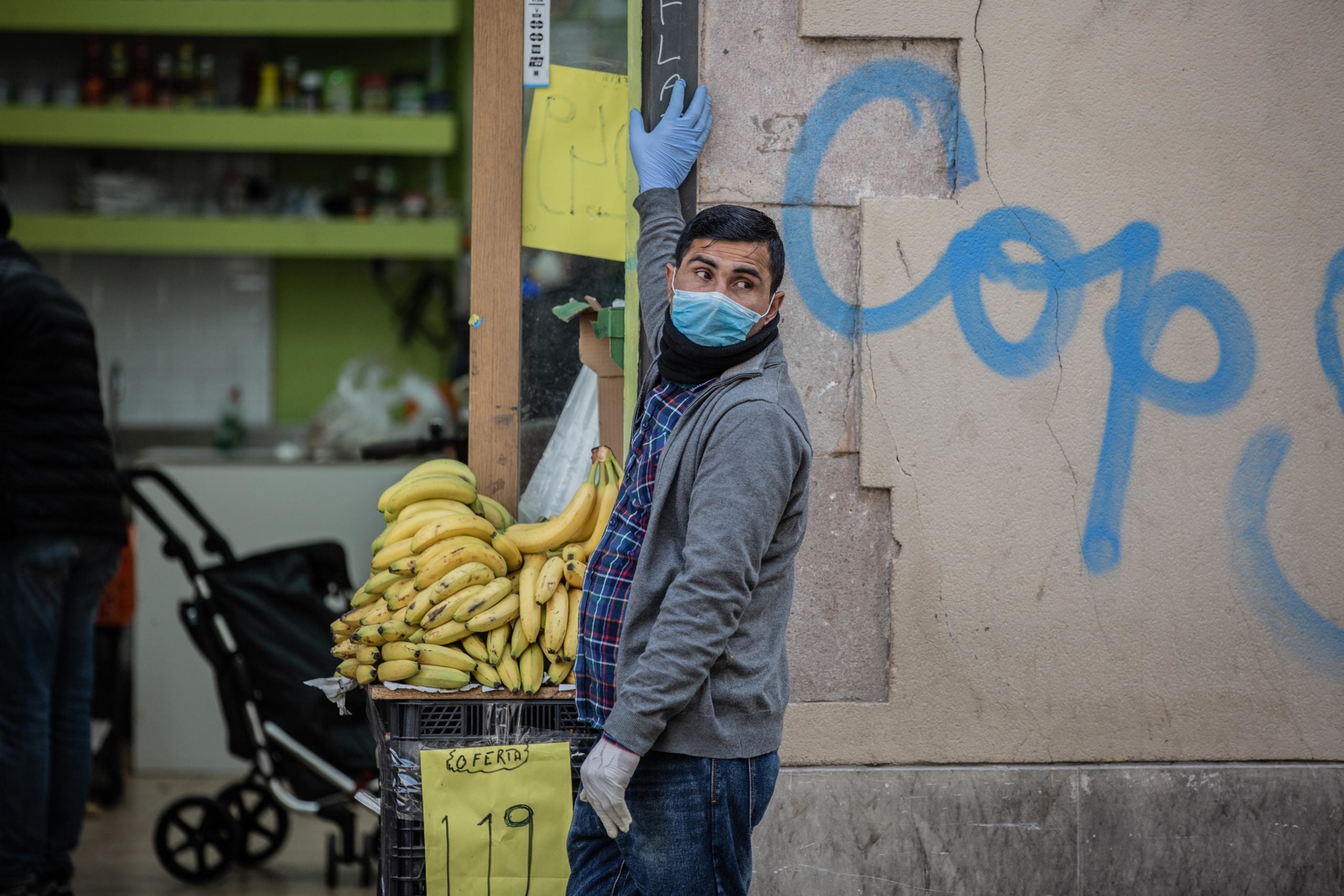 Un home protegit amb màscara i guants a la porta del seu establiment d'alimentació en el barri del Raval | EP