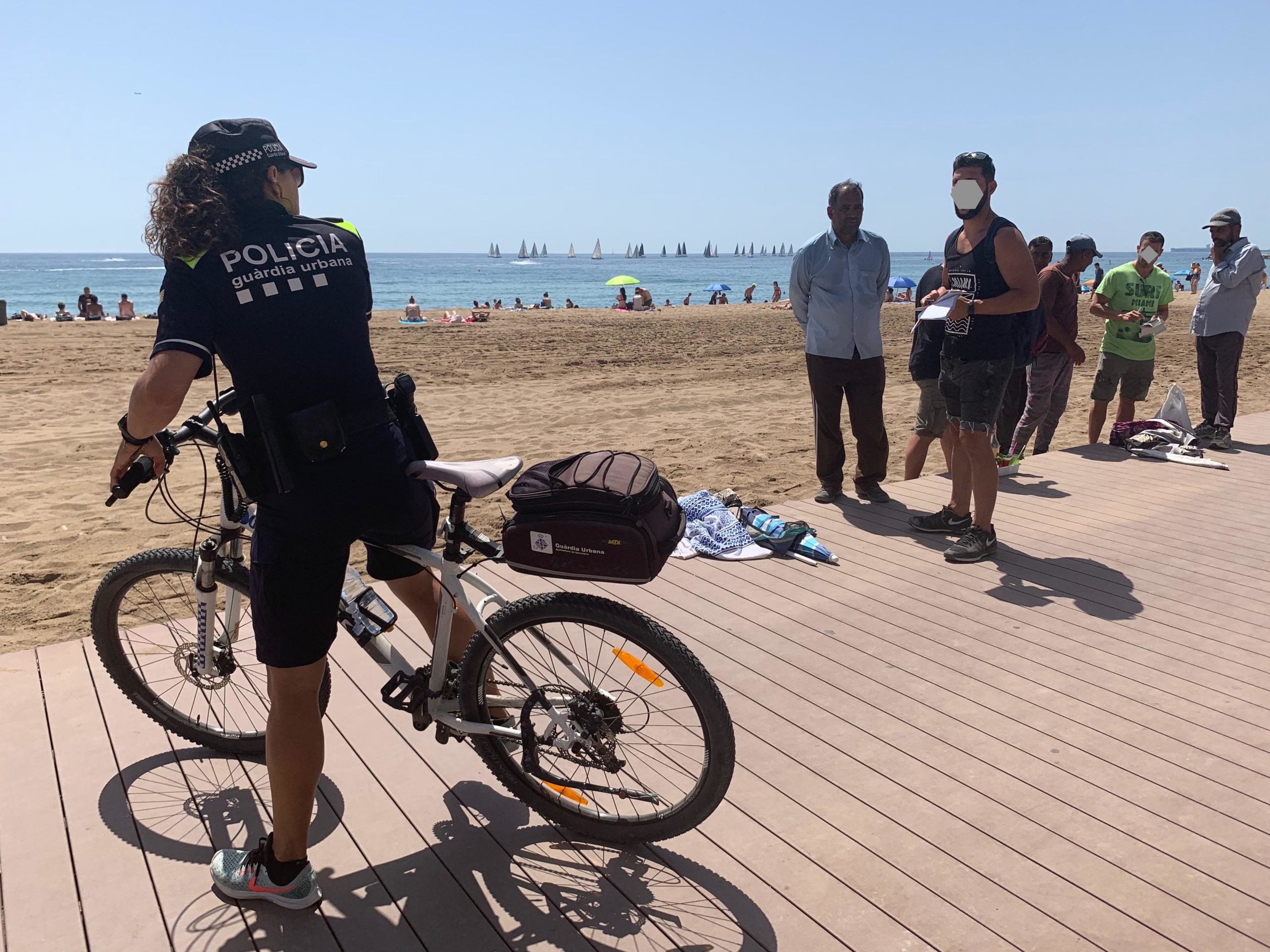 Una agent del grup de platges de la Guàrdia Urbana, amb bicicleta, parla amb companys seus de paisà, que han interceptat venedors ambulants sense llicència / S.B.