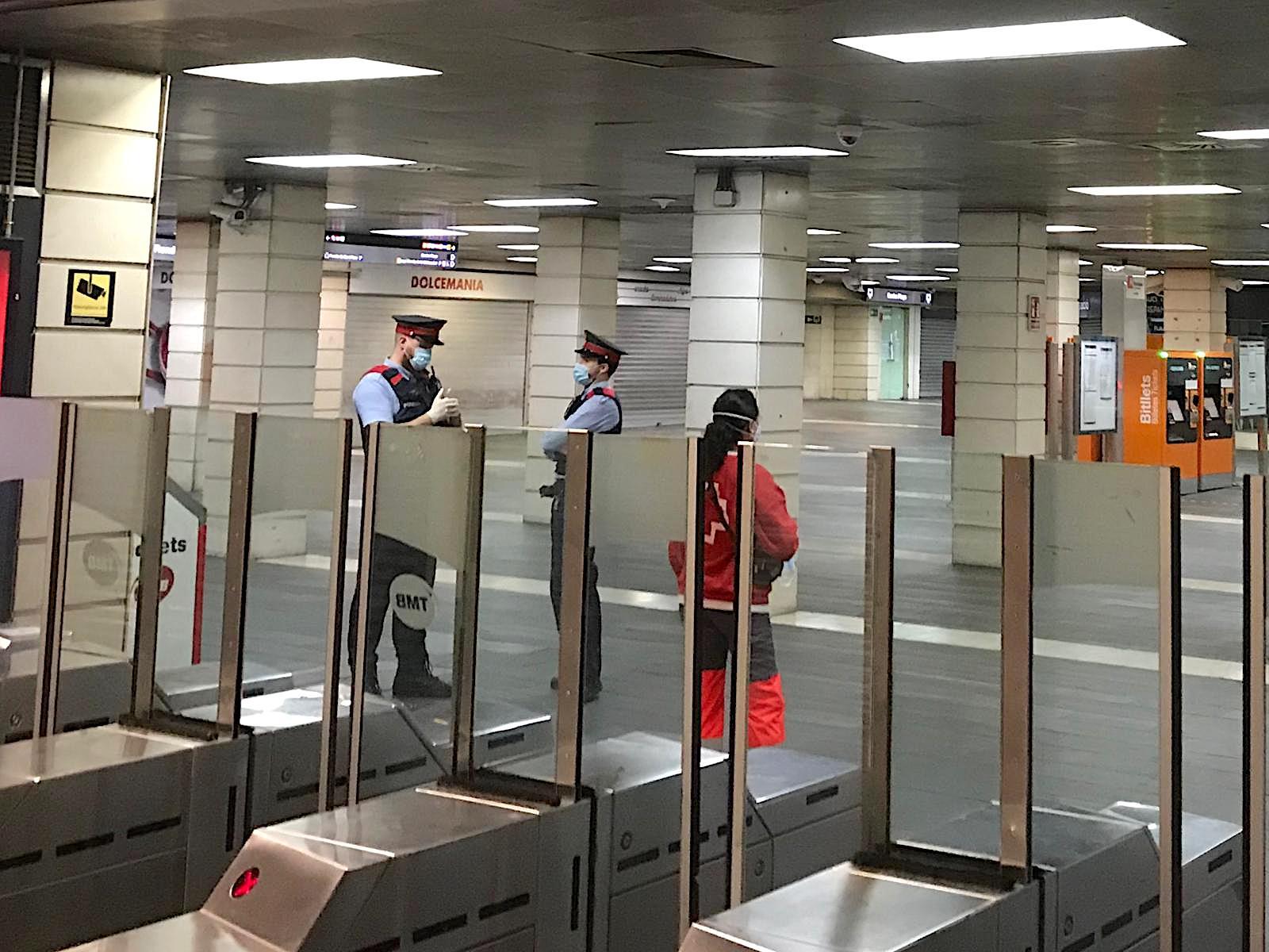 Dos agents dels Mossos i una voluntària de la Creu Roja que reparteix mascaretes al vestíbul de l'intercanviador de plaça Catalunya / A.G.