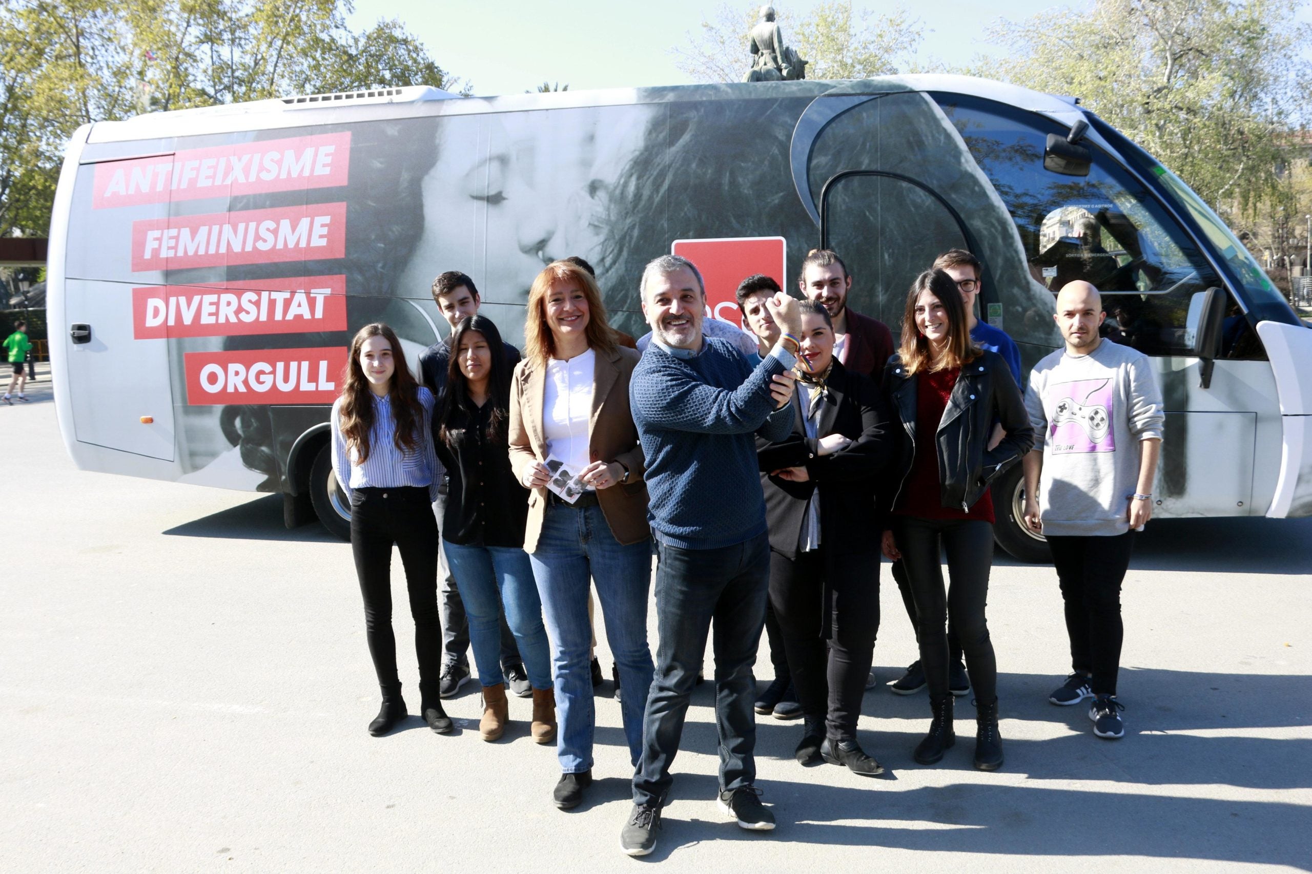 El candidat del PSC Jaume Collboni mostra una polsera amb els colors LGTB, amb la número 2, Laia Bonet, i joves del partit, davant l'autocar serigrafiat / ACN - Laura Fíguls