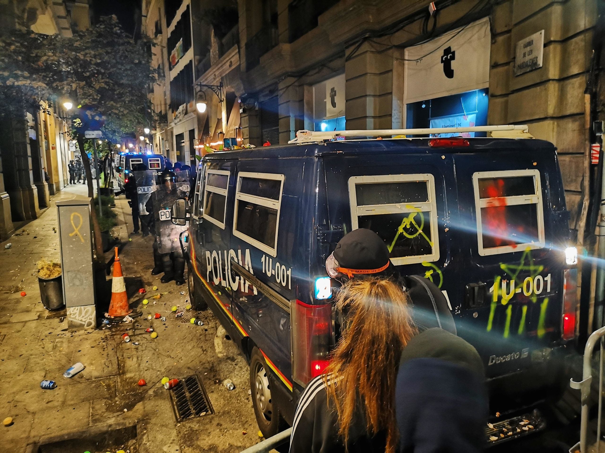 Furgons dels antiavalots de la Policia Nacional, pintats pels manifestants i envoltats de pilotes, a terra, al carrer de les Magdalenes, en la protesta convocada pels CDR per tornar les pilotes que han disparat / D.C.