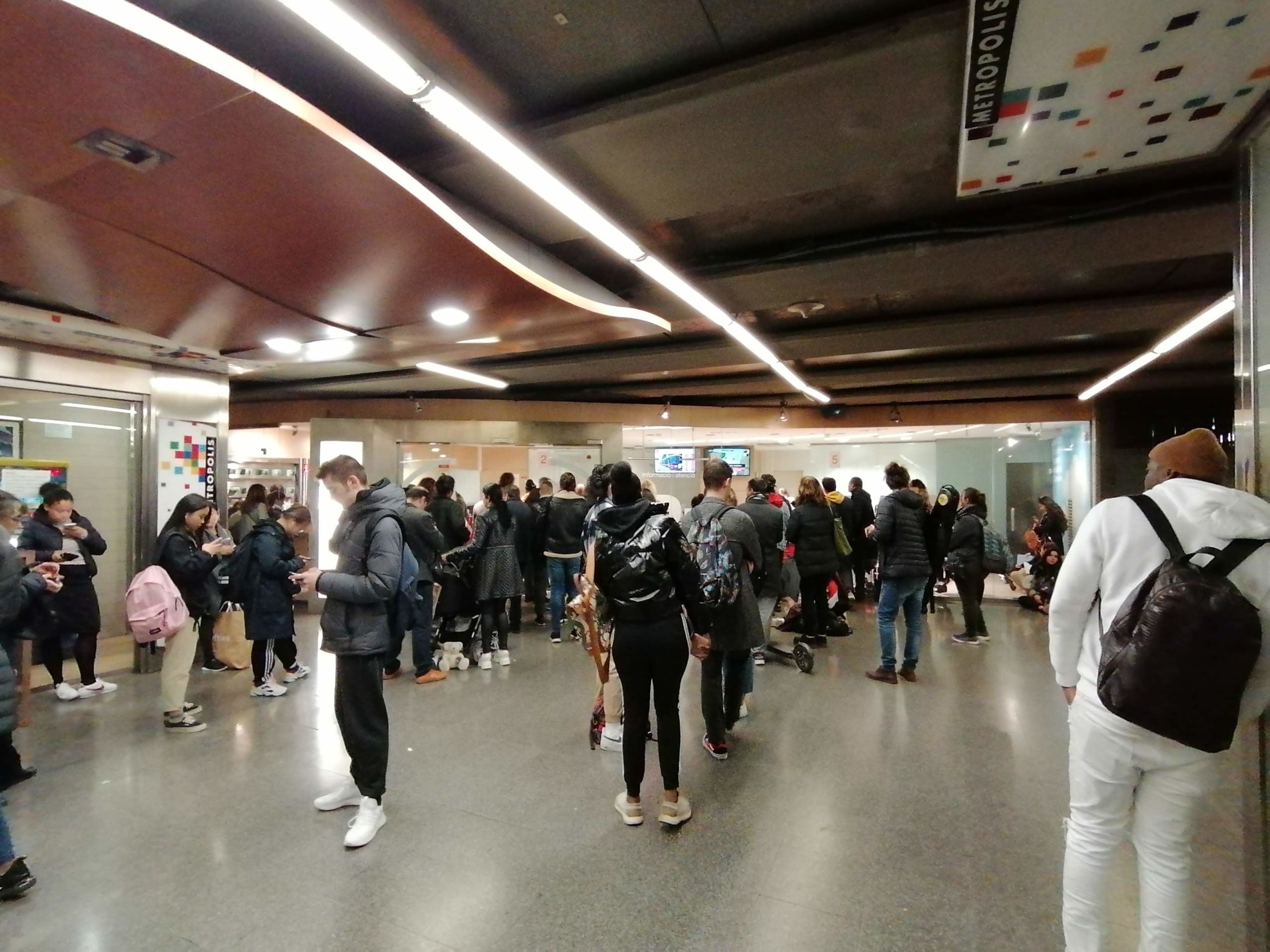 Vestíbul del metro Universitat ple d'usuaris que esperen tanda a l'oficina d'atenció / MMP