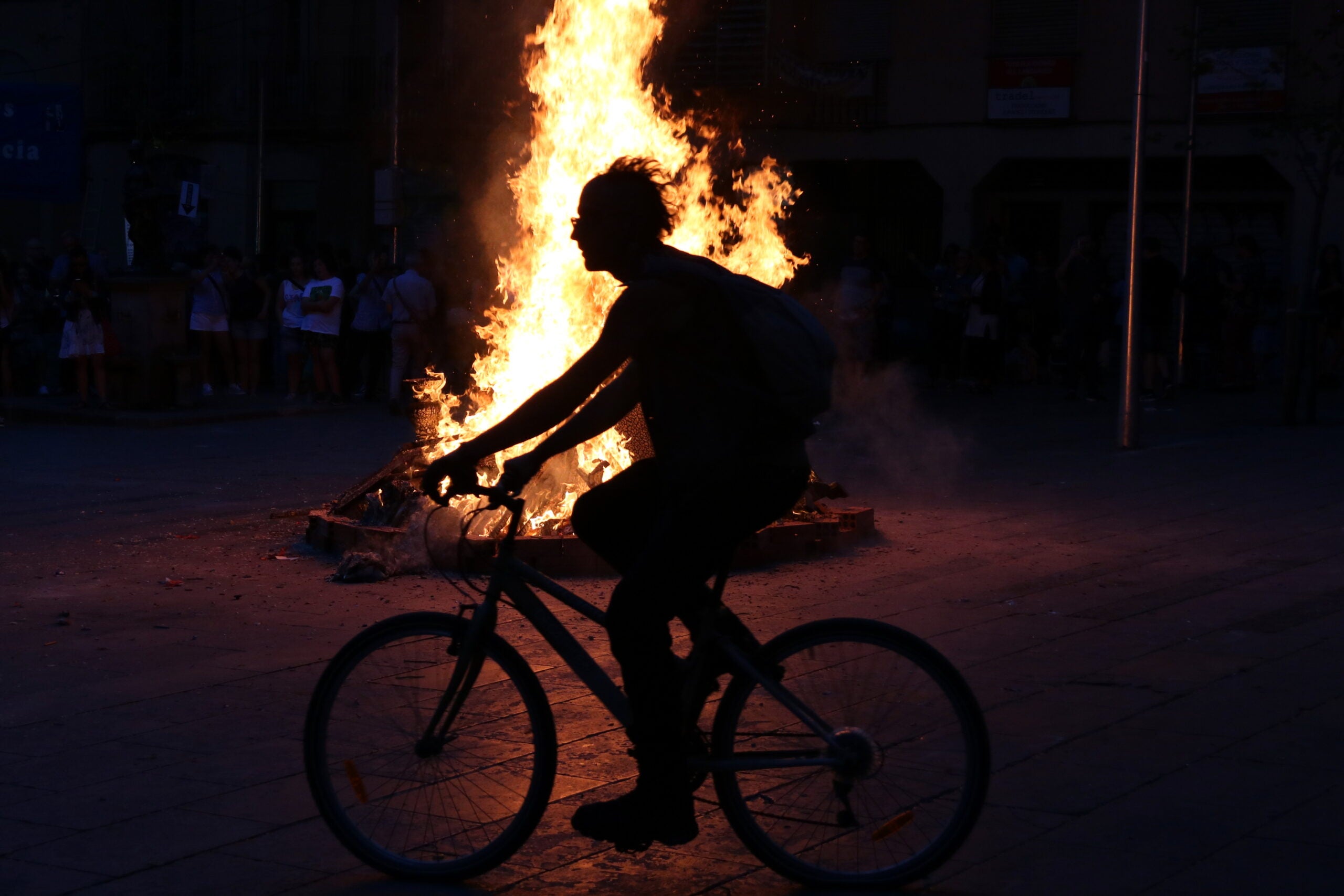 Contrallum d'una bicicleta passant per davant d'una foguera de Sant Joan a la plaça de la Virreina de Barcelona / ACN