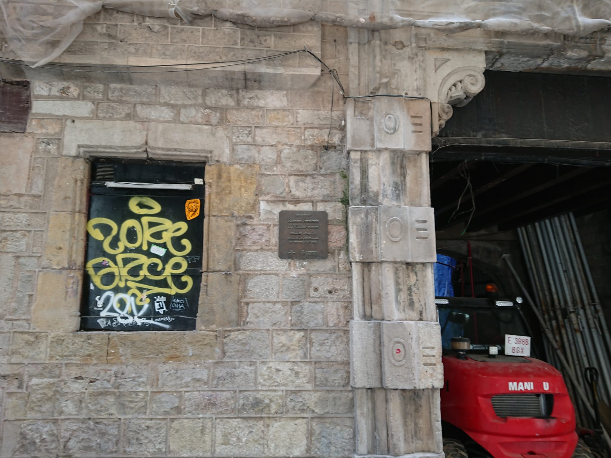 Placa a la façana, grafit i muntants de la porta sense protegir al palau Vilana-Perles, aquest juliol / Cedida 