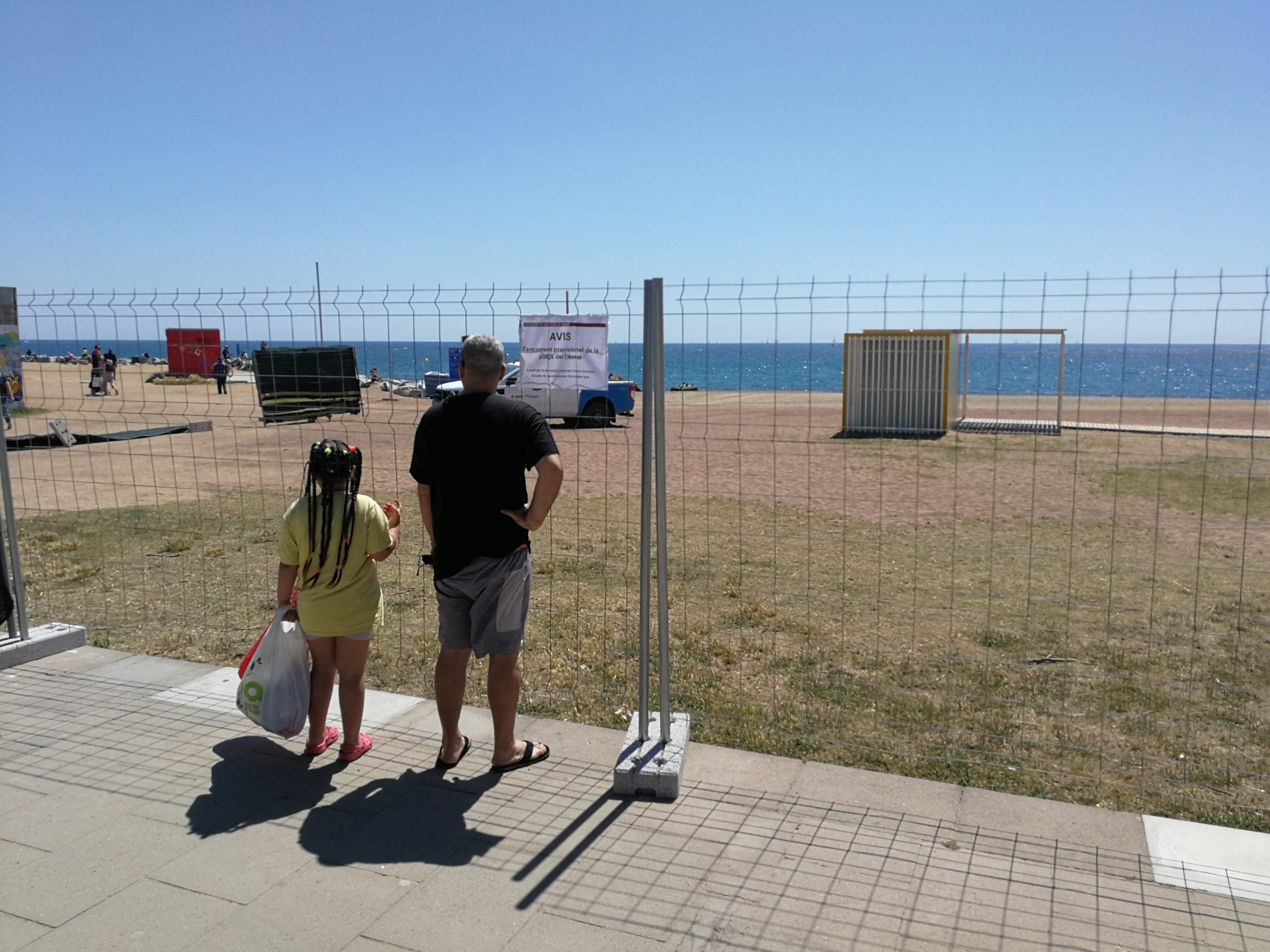 Dues persones llegeixen el cartell que informat del tancament de la platja de Sant Adrià del Besòs / TOT Barcelona