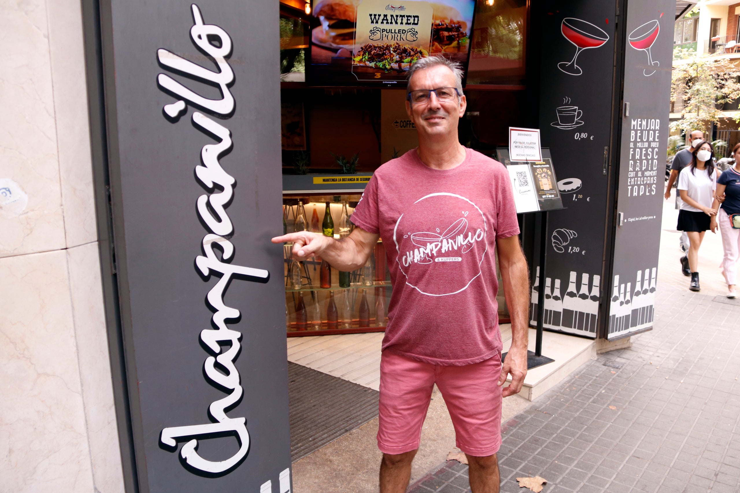 Un somrient David Iglesias, propietari del bar 'El Champanillo', assenyala el rètol al seu local a la plaça Doctor Letamendi / ACN