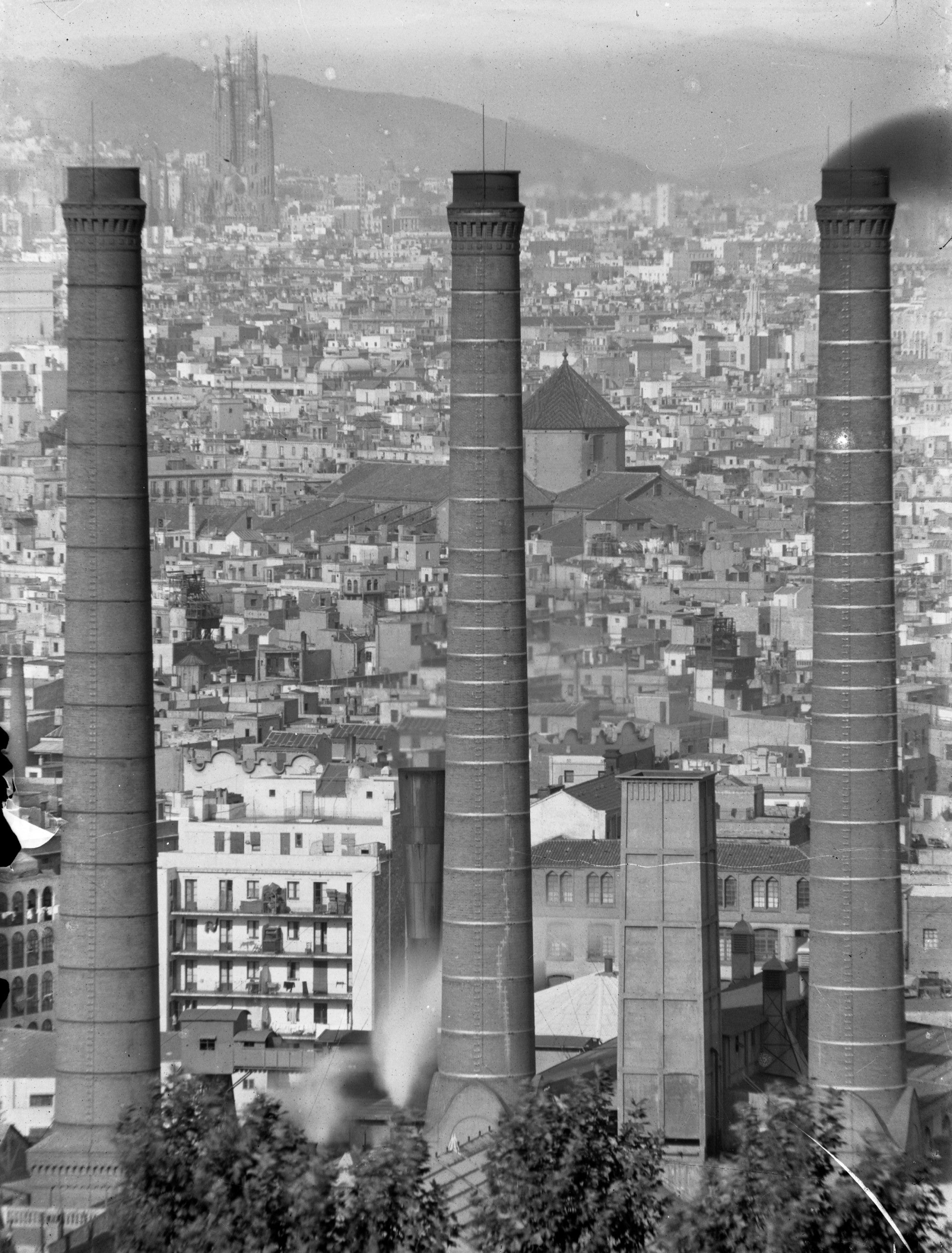 Vista de les tres xemeneies. Al fons, les quatre torres de la fatxada del Naixement del Temple Expiatori de la Sagrada Família on es poden observar les bastides. 1924 / Fons Històric (Fundació Endesa)