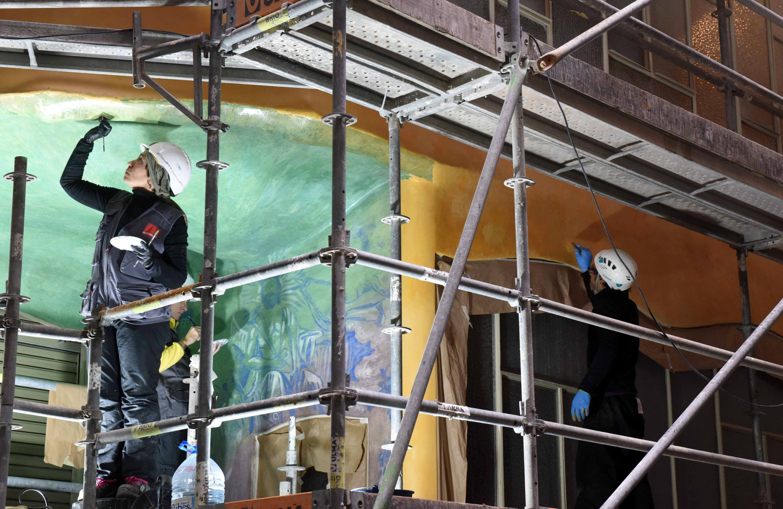 Dos restauradors, enfilats a la bastida durant la recuperació de les pintures murals del Pati de les Papallones, a la Pedrera / Marga Cruz