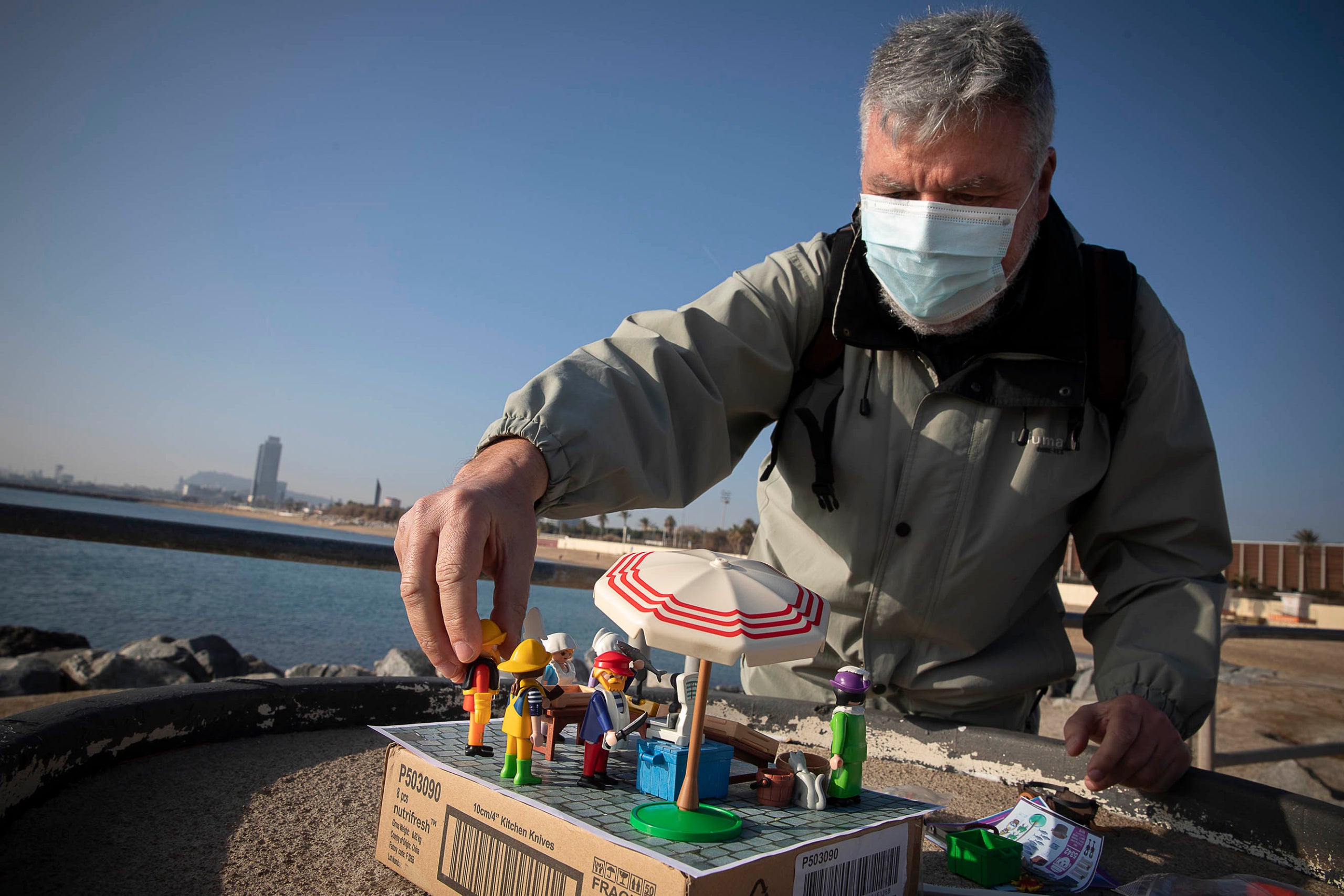 Paco Torres muntant l'escena amb ninos de Playmobil abans de fotografiar-la amb la costa de Barcelona de fons / Jordi Play