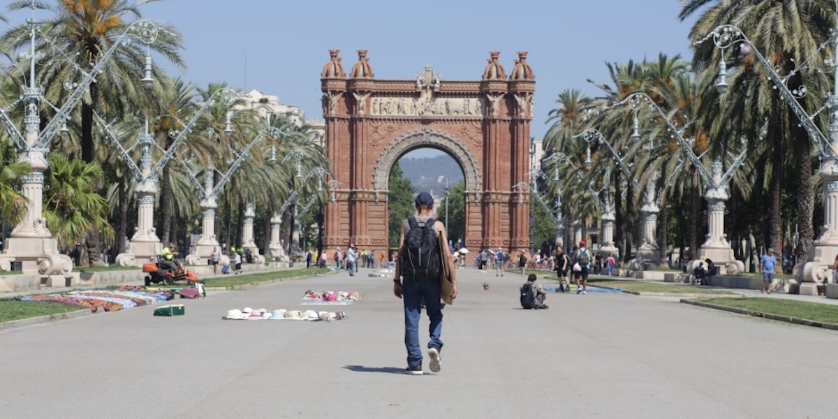 Una persona sense llar passeja sota el sol a Arc de Triomf | Arrels 