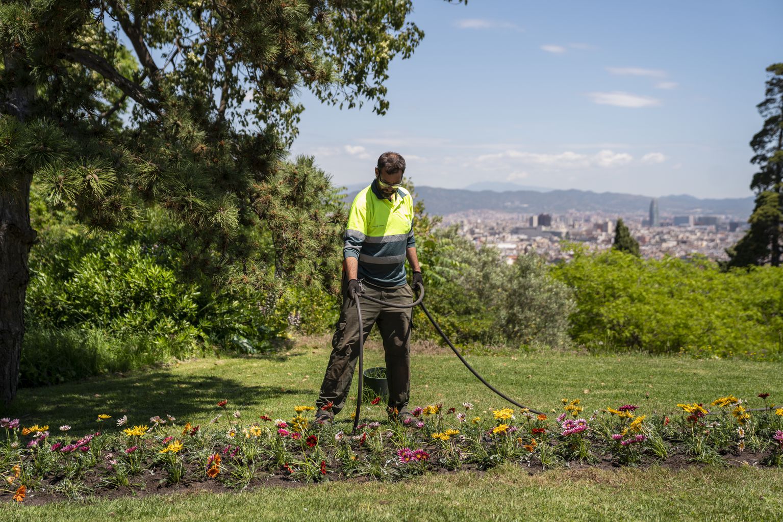 Un jardiner municipal rega un jardí des d'on es veu Barcelona | Ajuntament 