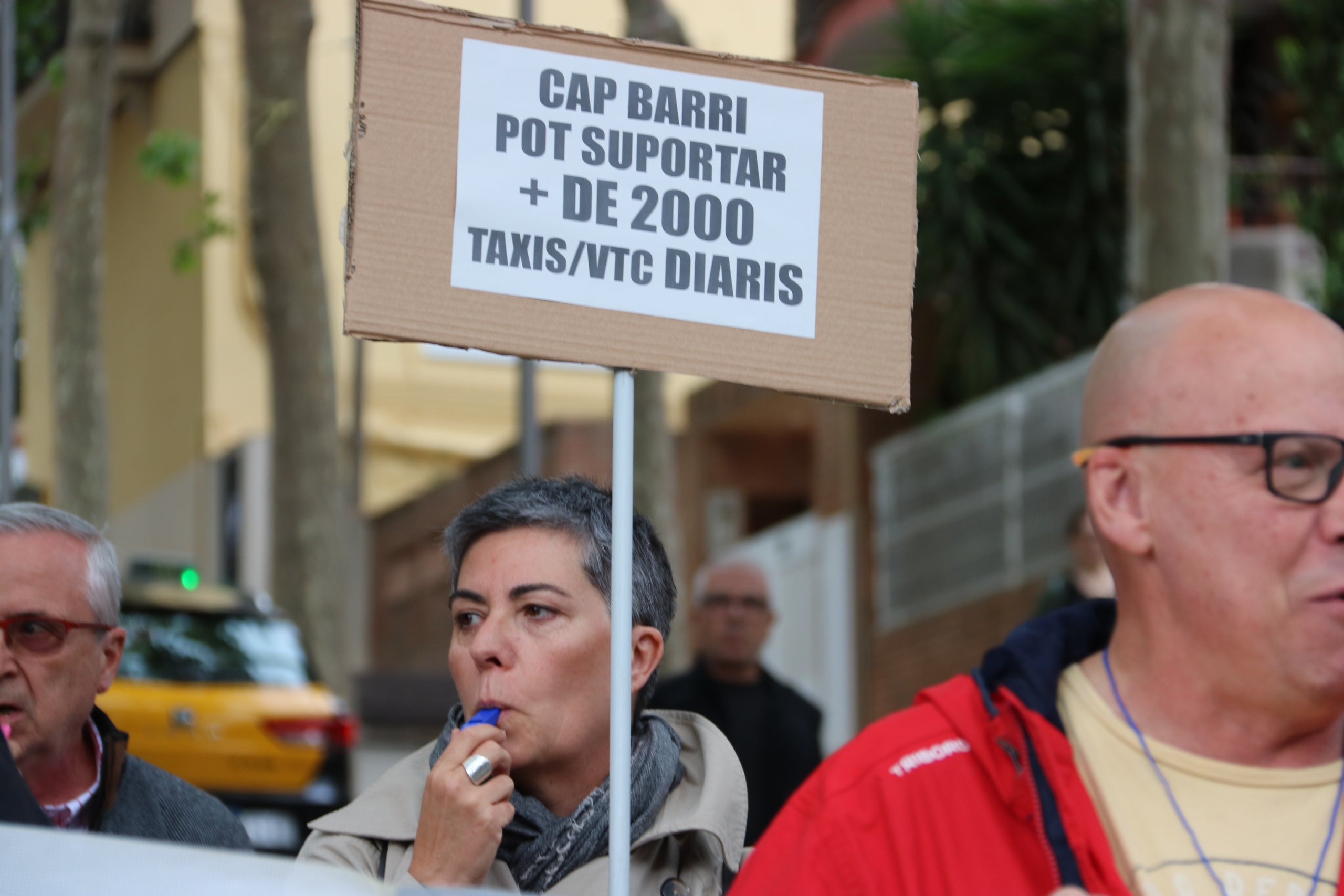Una de les veïnes del barri de la Salut de Barcelona xiulant i mostrant un cartell denunciant els taxis diaris que passen per la zona | Maria Aladern (ACN)