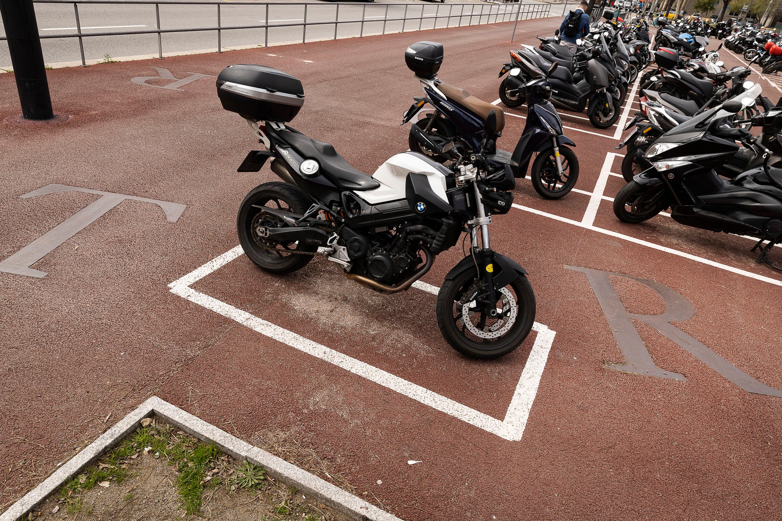 Motos aparcades a la plaça de Pau Vila, a la Barceloneta en un pàrquing ubicat al bell mig d'una escultura dels Jocs del 92 / Jordi Play