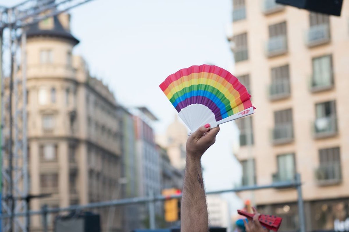 Una mà sosté enlaire un ventall amb els colors de la bandera LGTBI
