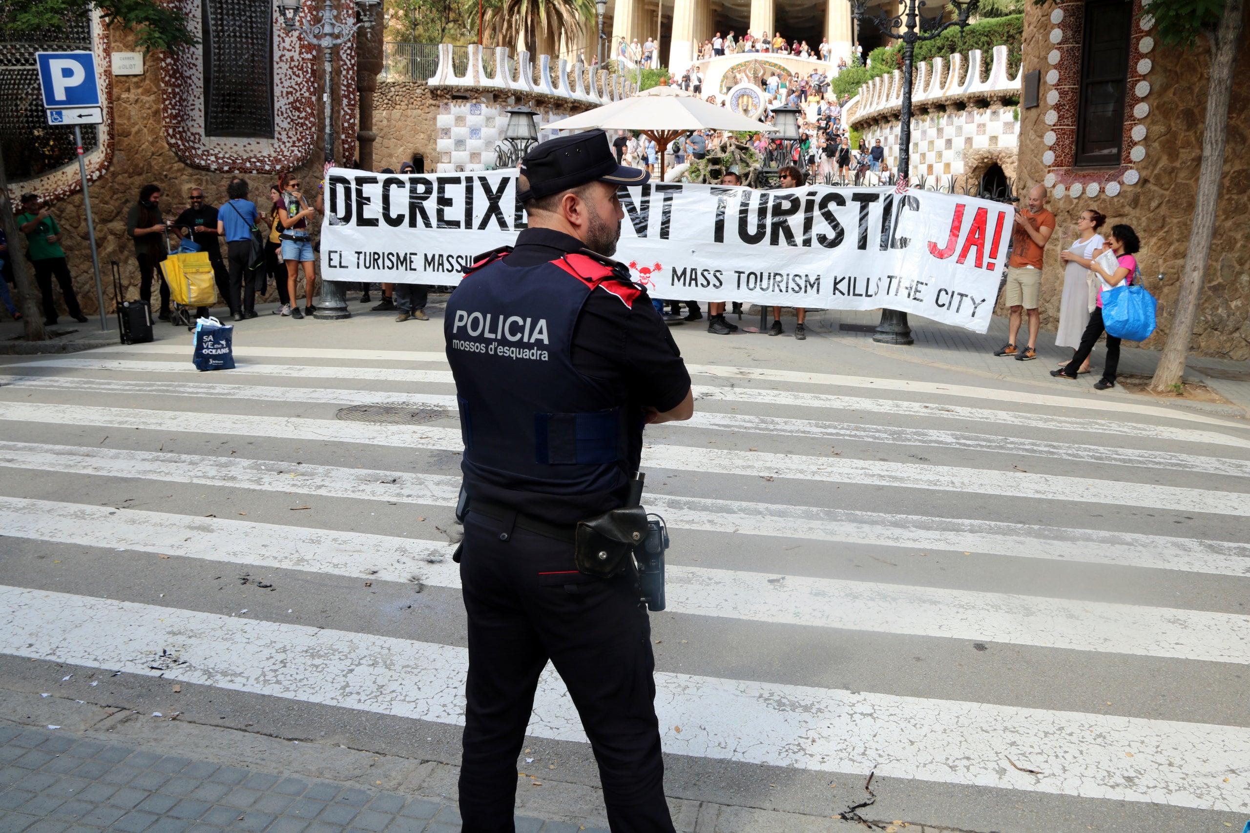 Un mosso observa la manifestació contra el turisme massiu a Barcelona que ha bloquejat una de les entrades del Park Güell | Jordi Bataller (ACN)