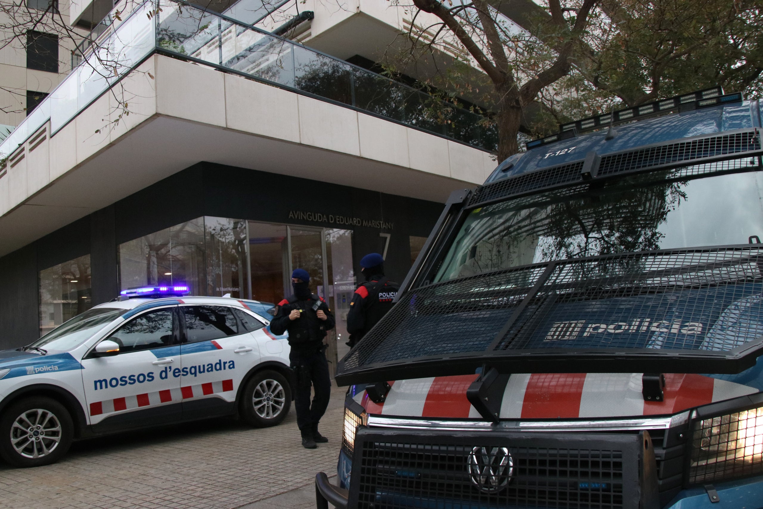 Els vehicles del cos dels Mossos a l'accés a l'edifici on s'ha escorcollat i detinguts a dues persones | Albert Hernàndez Ventós (ACN)