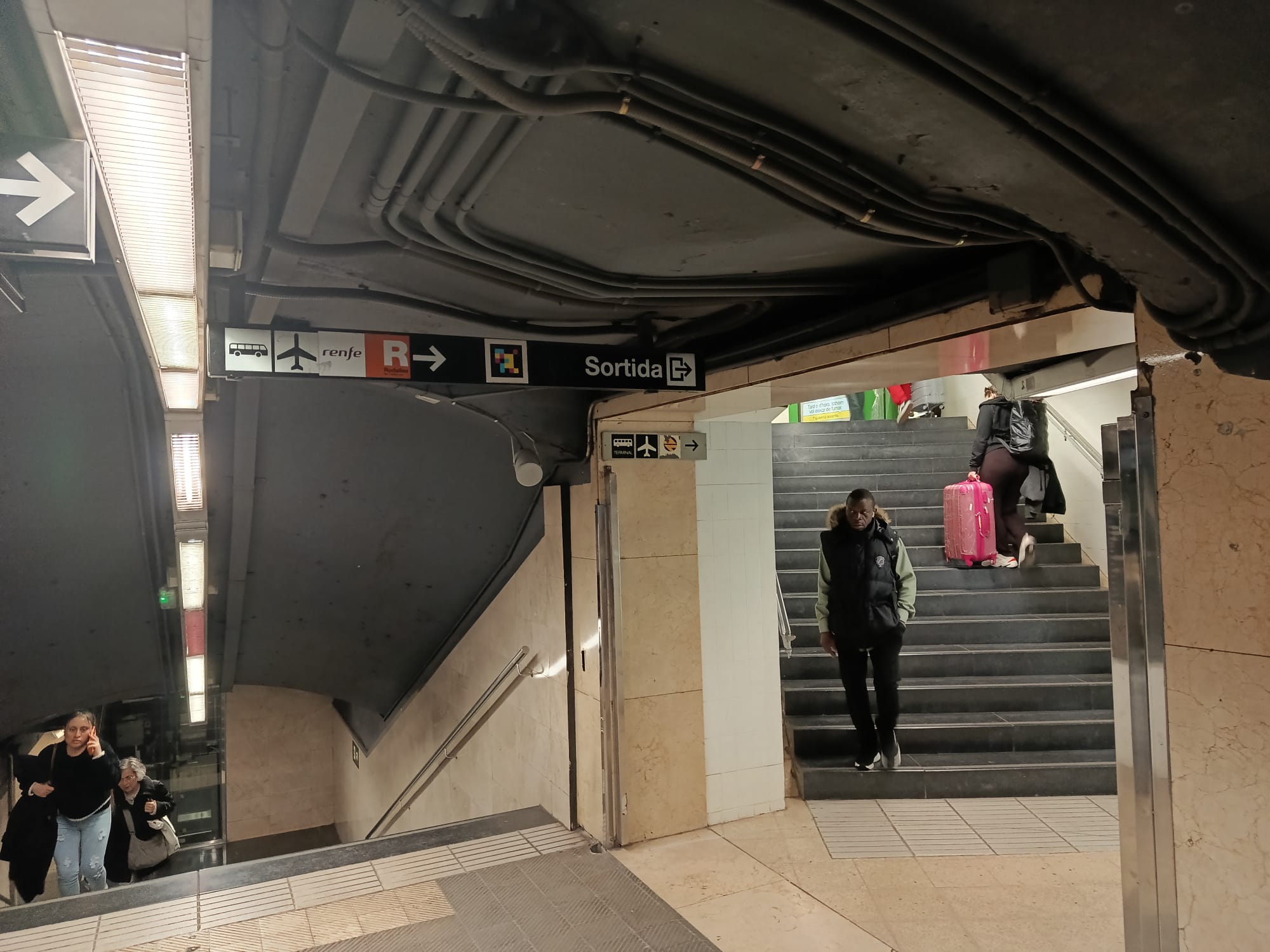 Passsatgers a l'estació de Sants amb un rètol que indica com anar a l'aeroport / Jordi Subirana 