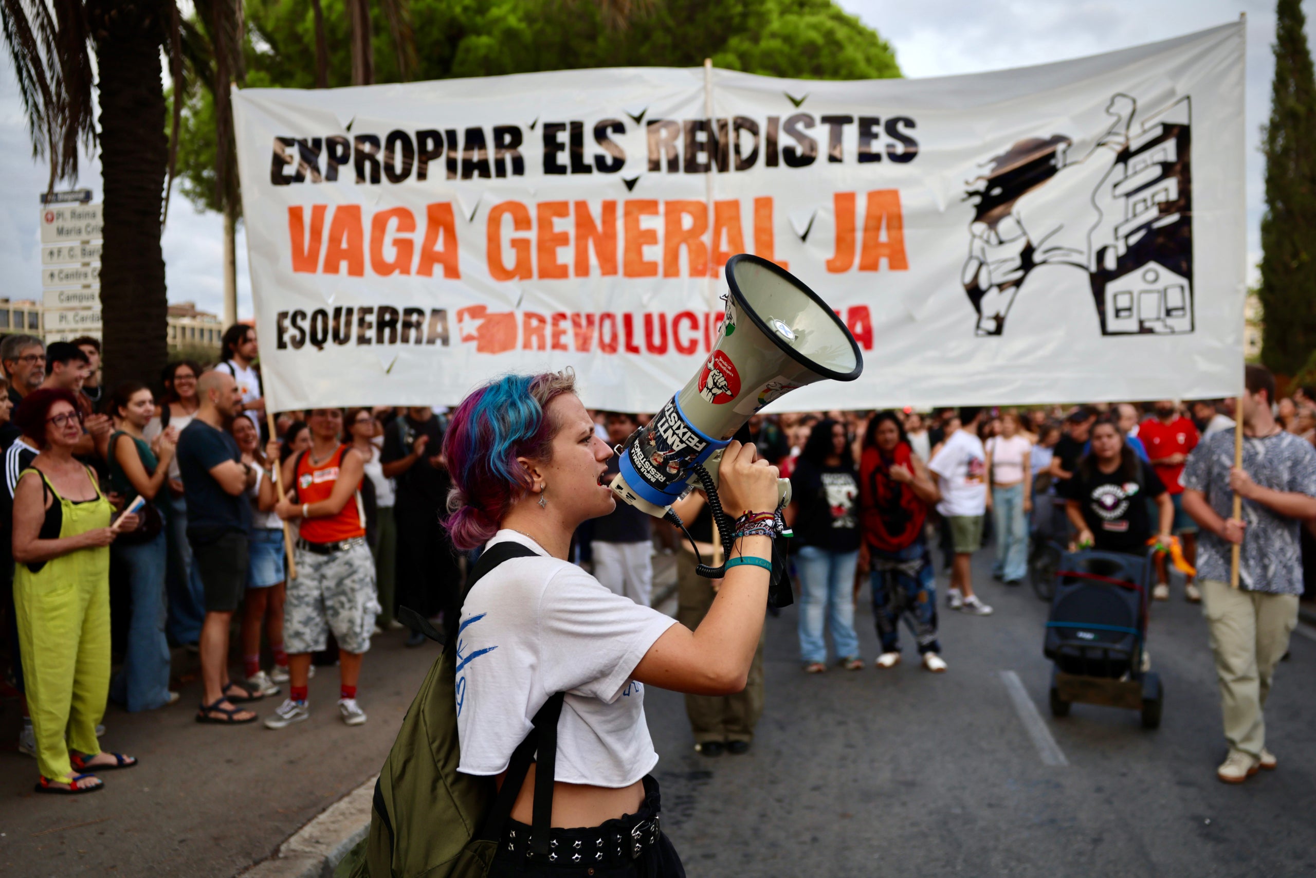 Una manifestant crida amb un megàfon a la protesta a la Diagonal de Barcelona per exigir solucions a la crisi de l'habitatge, davant una pancarta a favor de la vaga general / ACN