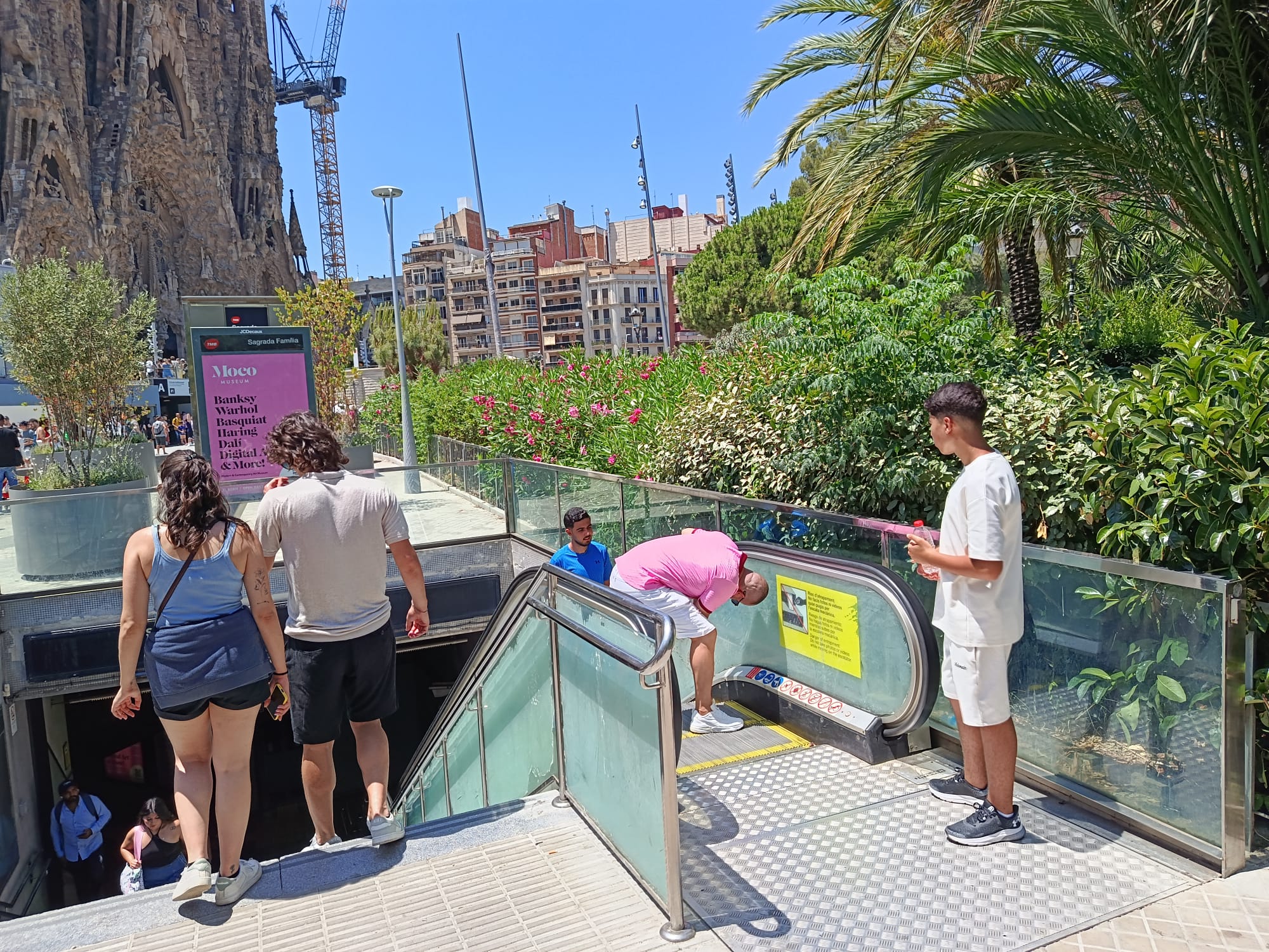 Uns turistes es fan fotos o vídeos al metro de la Sagrada Família, amb la basílica al fons, amb les escales mecàniques aturades, aquest dijous / Jordi Subirana